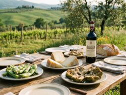Rustic Tuscan spring picnic with pecorino cheese, fresh fava beans, artichokes, bread and a bottle of Chianti set on a wooden table in the countryside.